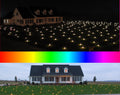 Lawn covered in small points of colored light in front of a house at night with a rainbow color bar