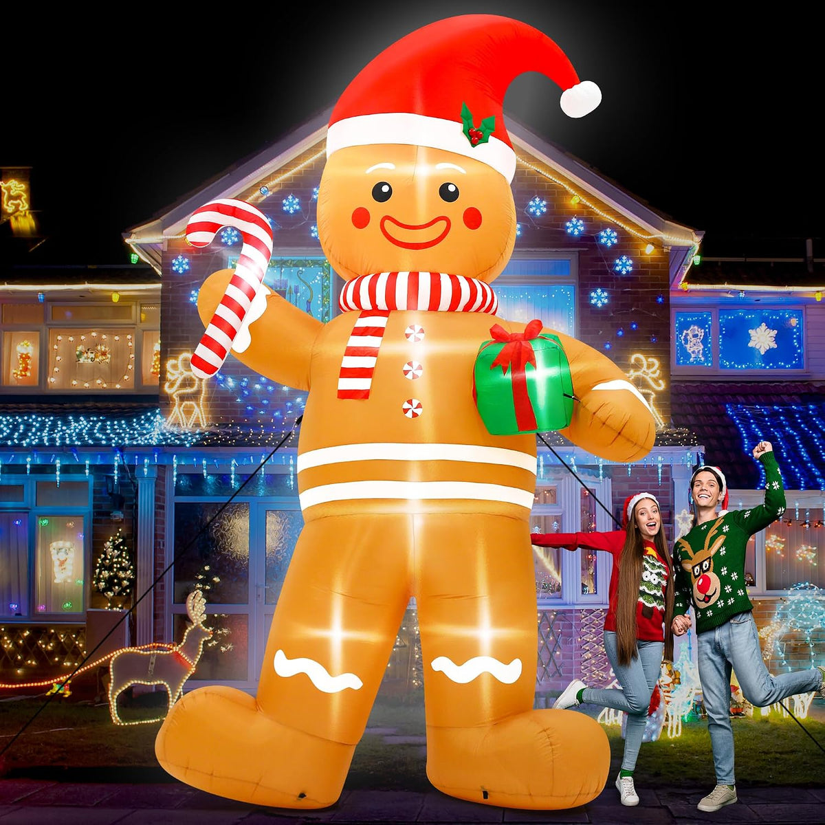 Giant gingerbread man inflatable in a Santa hat holding a candy cane and gift beside a posing couple