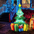 Small green Christmas tree inflatable with a gold star and colorful gifts at the base by a lit porch