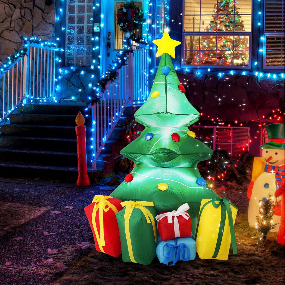 Small green Christmas tree inflatable with a gold star and colorful gifts at the base by a lit porch