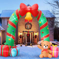 Candy cane striped arch inflatable with a red bow and gold bell over a front walk, gifts and a teddy bear below