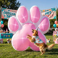 Giant pink and white paw print inflatable at a dog party with a golden retriever jumping beside it