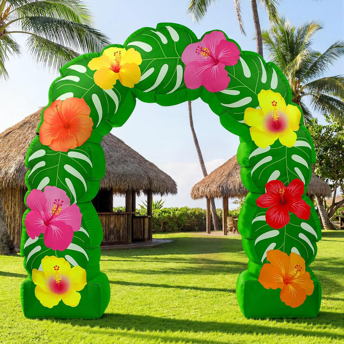 Green tropical arch inflatable covered in leaves and hibiscus flowers on a lawn with palm huts