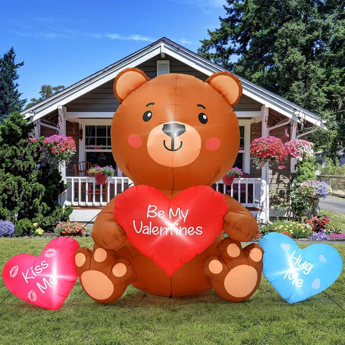 Big brown teddy bear inflatable holding a red Be My Valentine heart with pink and blue hearts on a lawn