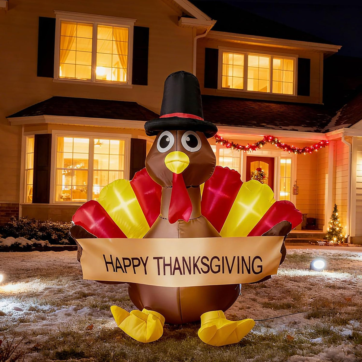Small turkey inflatable in a pilgrim hat holding a Happy Thanksgiving banner in front of a lit house
