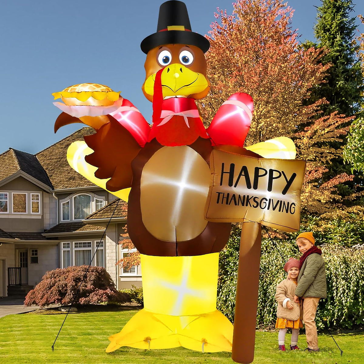 Tall turkey inflatable in a pilgrim hat holding a pie beside a Happy Thanksgiving sign and a family