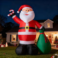 Giant Santa inflatable raising a candy cane with a green gift sack in front of a house at night